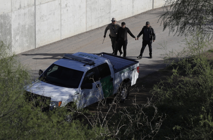 A U.S. Customs and Border Patrol agent walks with suspected immigrants caught entering the country illegally Wednesday along the Rio Grande in Hidalgo, Texas.