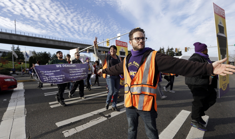 SEIU staffer Sam Finkelstein directs traffic as demonstrators march Tuesday at Sea-Tac airport. About 100 workers and supporters rallied nearby then circulated through the airport.