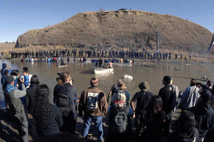 Dakota Access Pipeline protesters stand in the foreground and in the waist-deep water of the Cantapeta Creek, northeast of the Oceti Sakowin Camp, near Cannon Ball, N.D., on Wednesday. Officers in riot gear clashed again Wednesday with protesters near the Dakota Access pipeline, hitting dozens with pepper spray as they waded through waist-deep water in an attempt to reach property owned by the pipeline&#039;s developer.