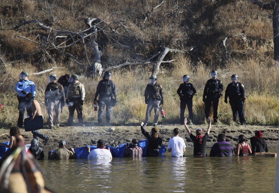 Protesters demonstrating against the expansion of the Dakota Access Pipeline wade in cold creek waters confronting local police as remnants of pepper spray waft over the crowd near Cannon Ball, N.D. The U.S. Army Corps of Engineers says it&#039;s trying to diffuse tensions between pipeline protesters and law enforcement in North Dakota, but that the pipeline&#039;s developer isn&#039;t cooperating. (AP Photo/John L.