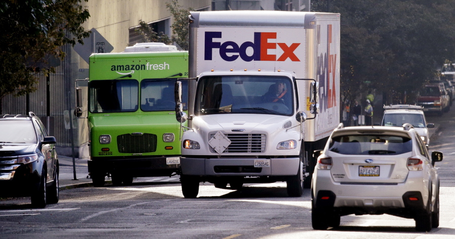 A FedEx truck drives past an AmazonFresh truck already taking up the loading zone space only to park in a traffic lane on a downtown street in Seattle.