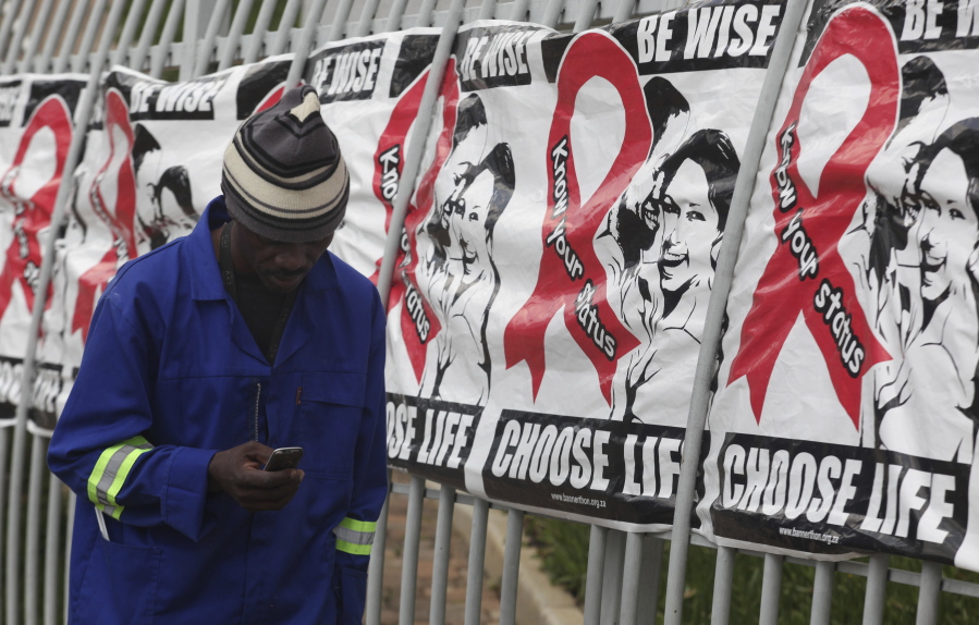 FILE -- In this Dec. 1, 2014 file photo a man makes a call on a mobile phone as he passes World AIDS Day banners on the perimeter of an office building in Sandton, Johannesburg, South Africa.  A new vaccine against HIV, called HVTN 702, is to be tested in South Africa, it is announced Sunday Nov. 27, 2016, and scientists aims to enroll 5,400 sexually active men and women for the clinical trial.