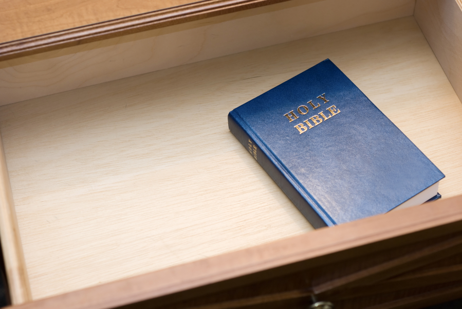 A Bible sits in a hotel room nightstand open drawer.