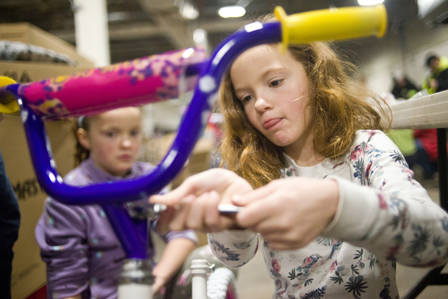 Simone Ranta, 7, tightens down a handle bar while assembling a bike with her twin sister, Estelle, during a bike building event at the Columbia Machine warehouse on Thursday. Waste Connections organized the event, with a goal of building 616 bikes for various organizations to distribute before Christmas.