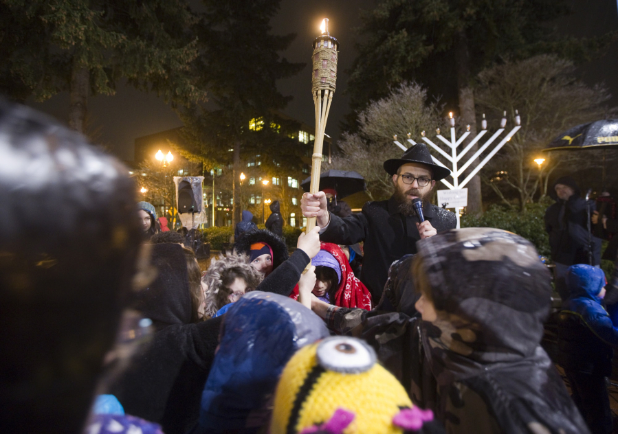 Rabbi Shmulik Greenberg holds a torch to light a menorah Monday evening at a Hanukkah celebration for the community in Esther Short Park in Vancouver. Rabbi Greenberg asked the children to join him in singing a song and holding the torch.