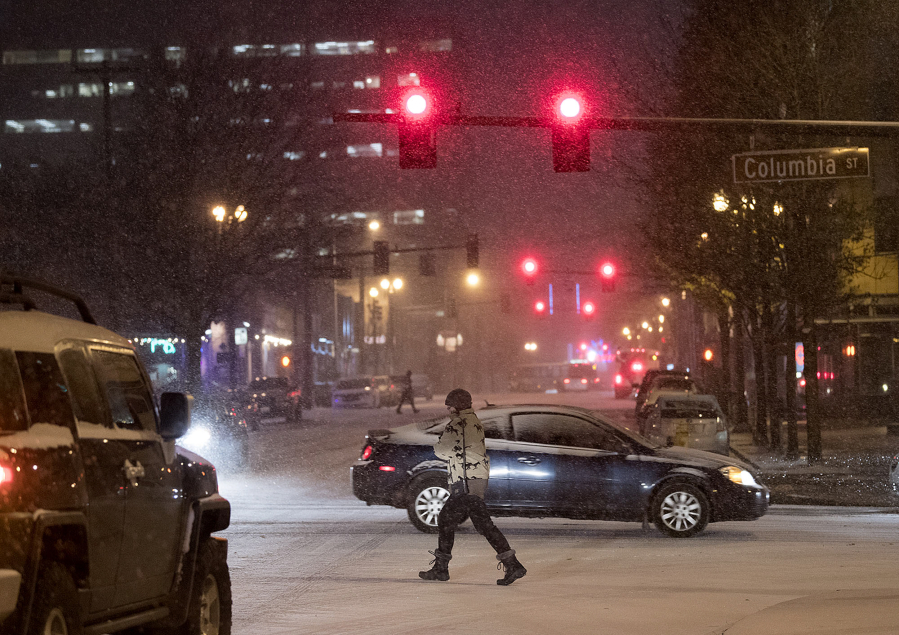 Pedestrians and motorists navigate through downtown Vancouver in the snow Wednesday evening.