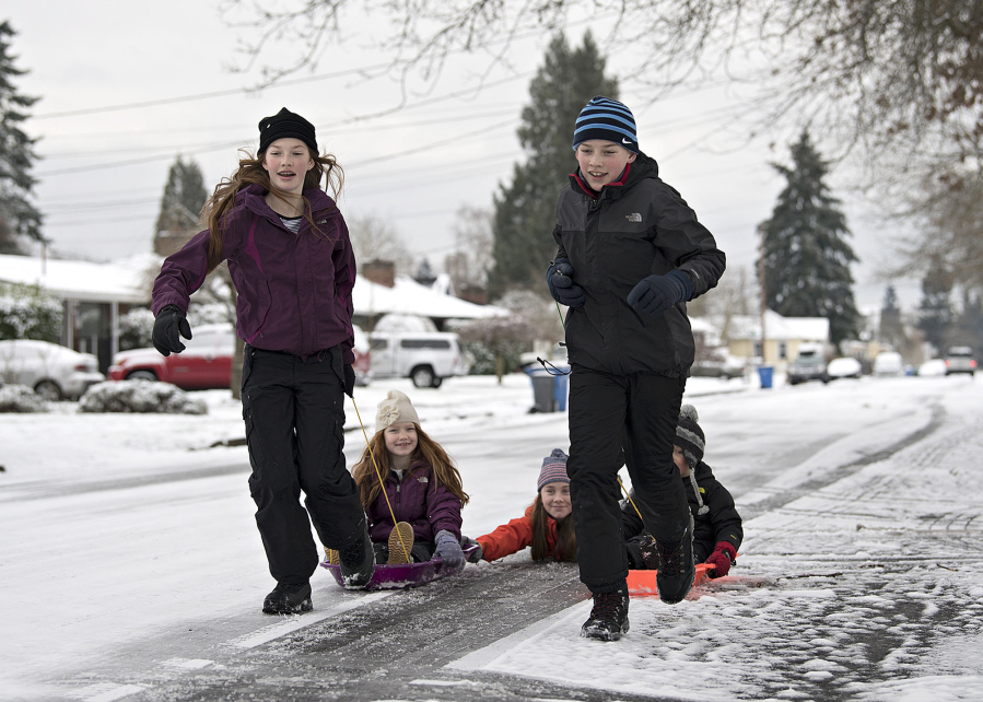 Grace Hopkins, 13, left, enjoys the winter weather Thursday afternoon with Maggie Hopkins, 7, Julia Blevins, 13, Tate Hopkins, 12, and Finley Reudink, 5, on the sled to the right, while they make their way along a slick Northwest Daniels Street.