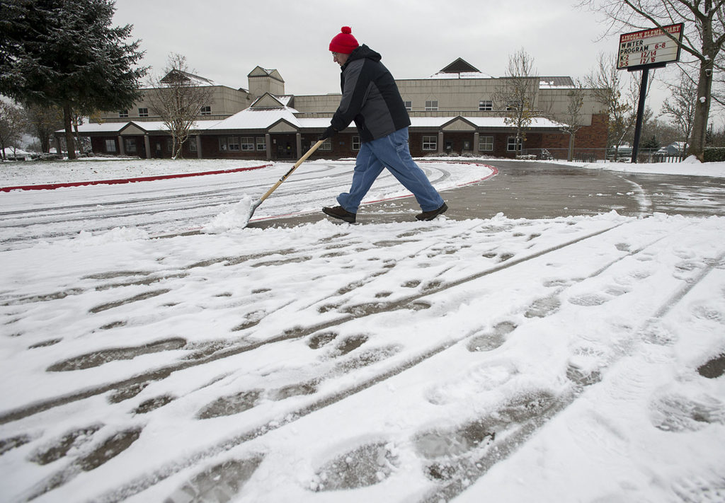 Lincoln Elementary School building operator Gene Boyer clears the sidewalk outside the school as snowy footprints are seen nearby Thursday afternoon, Dec. 15, 2016.