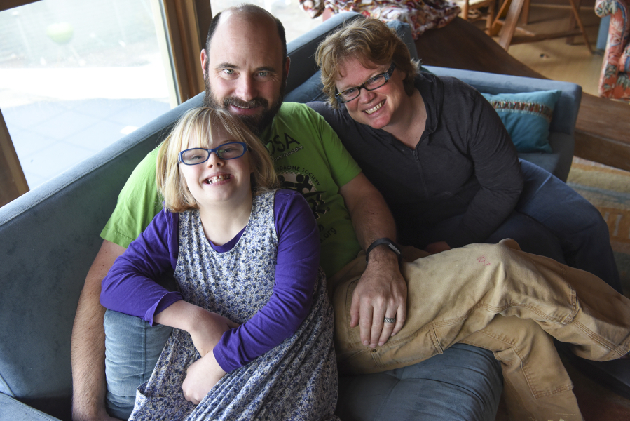 Adara Morgan, 10, who has Down syndrome, left, snuggles on the couch with her parents, David Morgan, center, and Abby Braithwaite, at their home in Ridgefield on Friday.