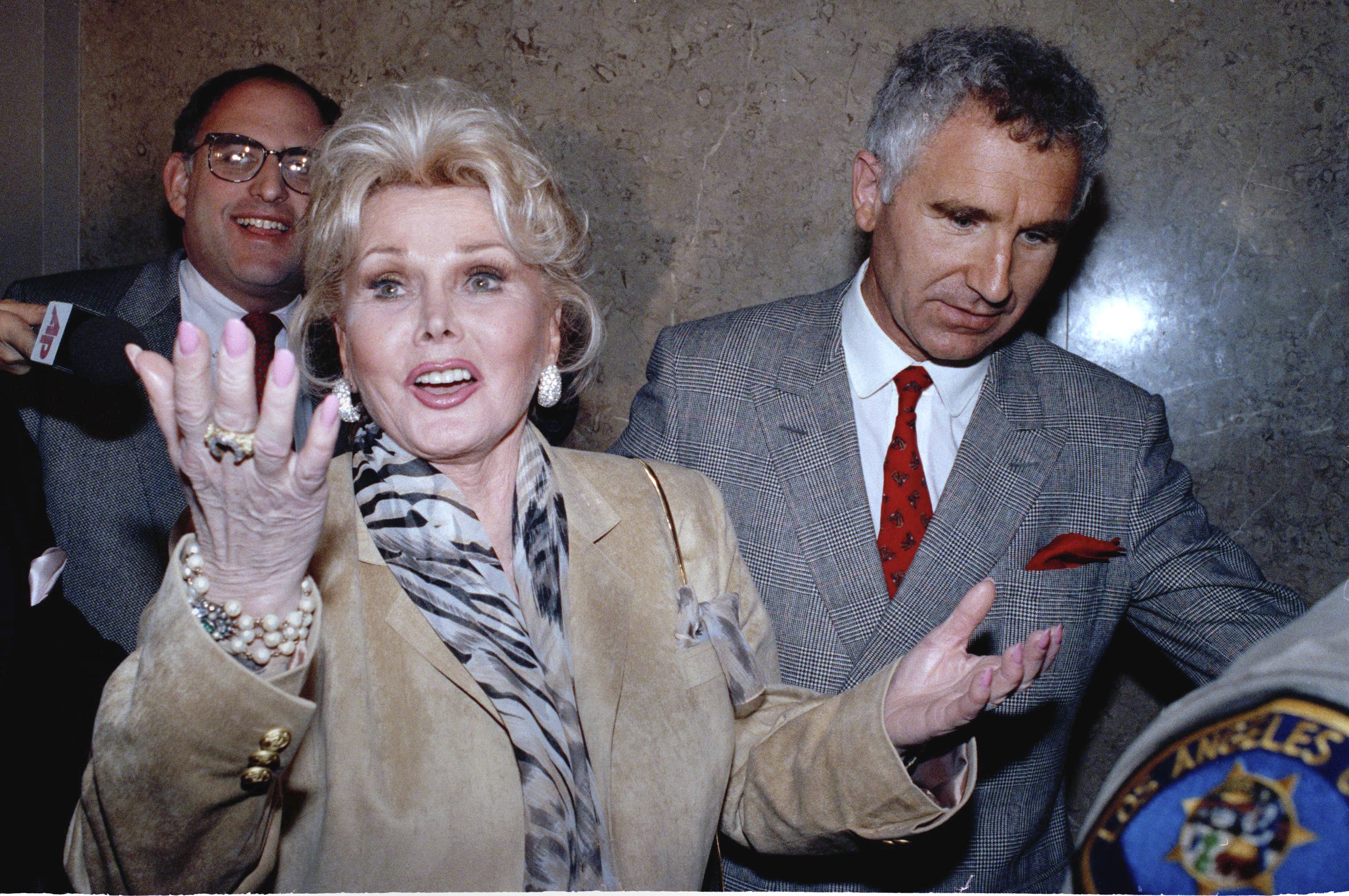 In a May 1, 1990 file photo, Zsa Zsa Gabor gestures as she while answering questions as she leaves the Beverly Hills courtroom where judge Charles Rubin ruled that she violated her probation. Gabor was ordered to complete her community service at a Venice homeless shelter, with an additional 60 hours. At right is her husband Frederick von Anhalt. Gabor died Sunday, Dec. 18, 2016, of a heart attack at her Bel-Air home, her husband, Prince Frederic von Anhalt, said.