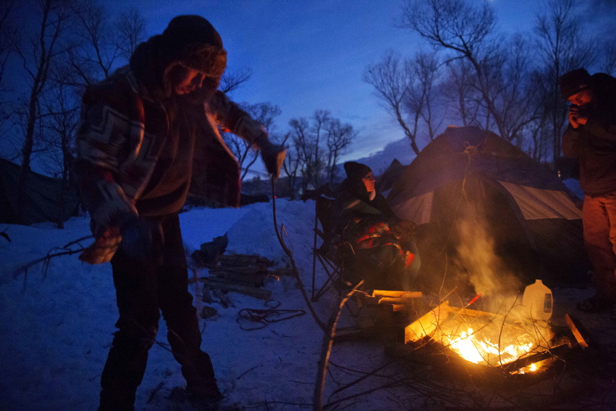 From left, Kaleb Grady, Donna Grady, and Jordan Jumping Eagle, all Dakota Native Americans from Rapid City, S.D., keep a fire going outside their tent at Oceti Sakowin camp where people have gathered to protest the Dakota Access oil pipeline in Cannon Ball, N.D., Saturday, Dec. 3, 2016.
