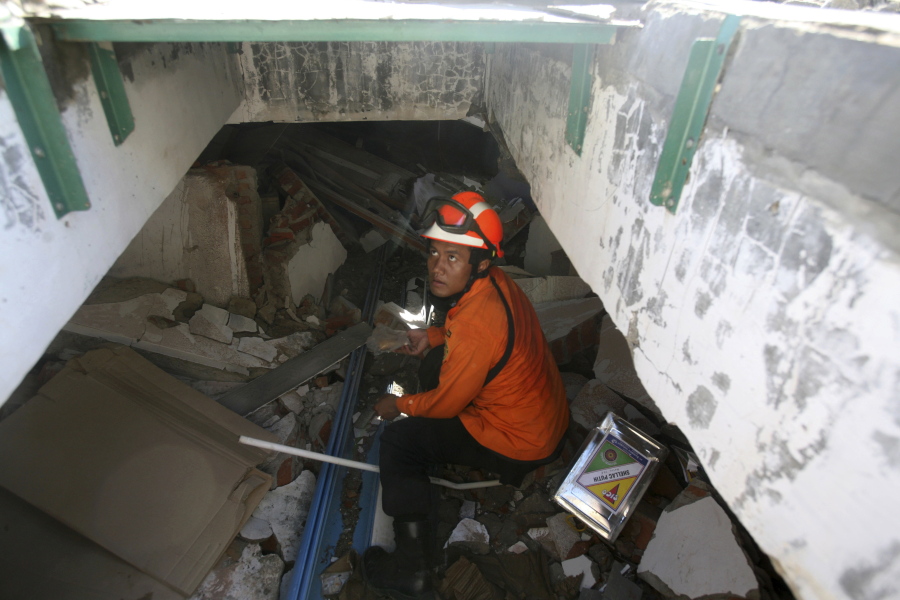 A rescuer searches for victims under the rubble of a collapsed market Thursday in Meureudu, Indonesia.