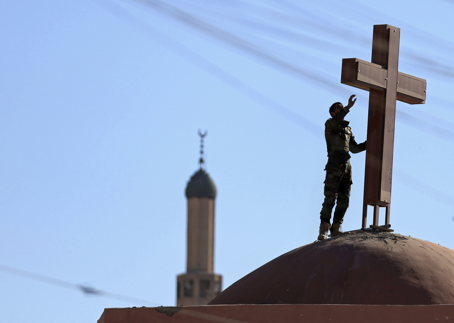 An Iraqi Kurdish peshmerga fighter sets a cross on top of a church Wednesday in Bashiqa, east of Mosul, Iraq. The church was damaged by Islamic State during their occupation.