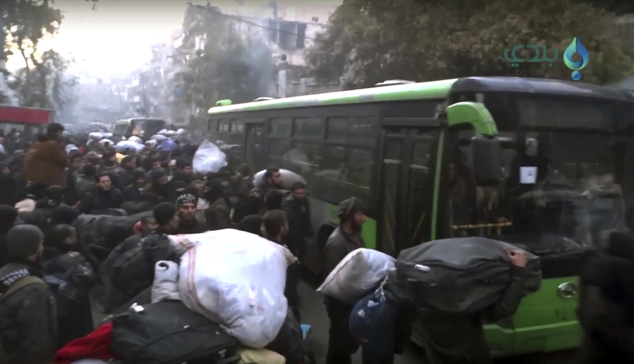 This image from video provided by Baladi News Network, a Syrian opposition media outlet, shows residents gathering Thursday near green government buses for evacuation from eastern Aleppo, Syria.