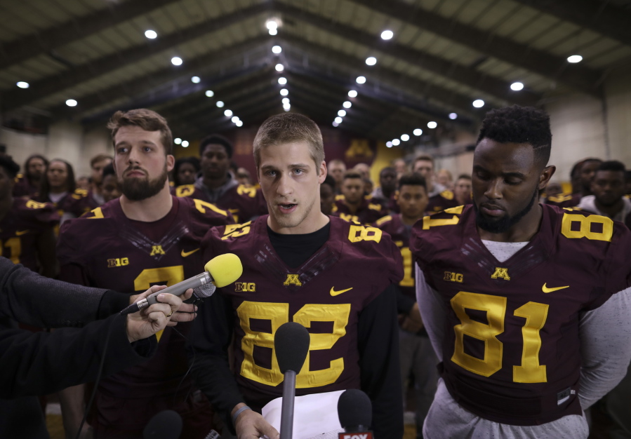 Minnesota wide receiver Drew Wolitarsky, flanked by quarterback Mitch Leidner, left, and tight end Duke Anyanwu stands in front of other team members as he reads a statement.  The players delivered a defiant rebuke of the university&#039;s decision to suspend 10 of their teammates, saying they would not participate in any football activities until the school president and athletic director apologized and revoked the suspensions.