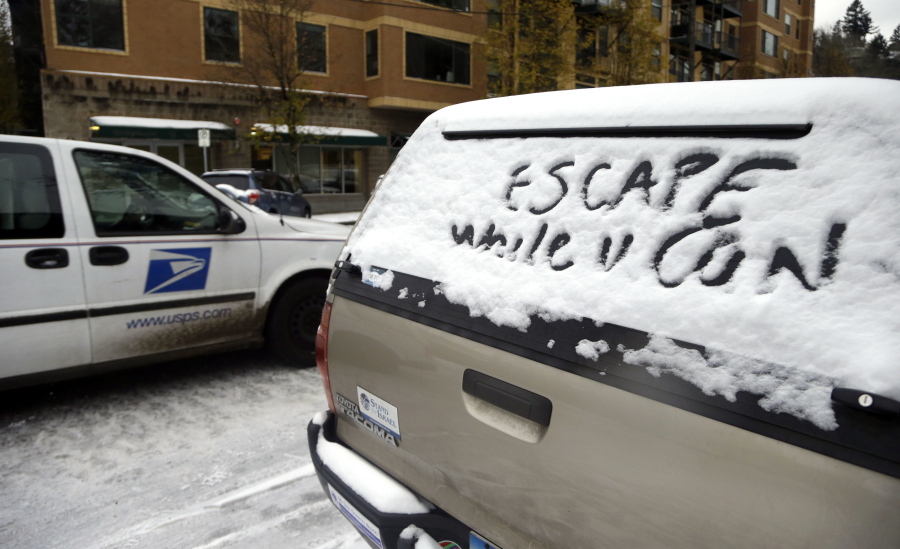 A postal truck passes a car with a warning written in snow in a rear window Thursday in Portland.