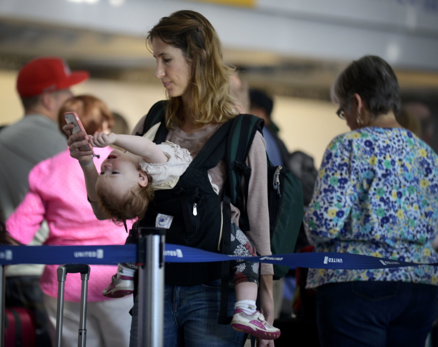 Ann Walden checks her phone as 15-month-old daughter Delphine plays while waiting in line after their flight was delayed Sept. 26, 2014, at O&#039;Hare International Airport in Chicago. There are several ways to distract and soothe little ones when traveling by air.