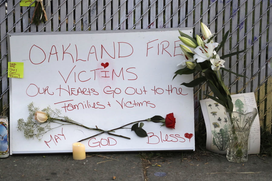 Signs and flowers adorn a fence near the site of a warehouse fire Monday in Oakland, Calif. The death toll in the Oakland warehouse fire on Friday climbed Monday with more bodies still feared buried in the blackened ruins, and families anxiously awaited word of their missing loved ones.