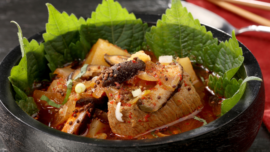 Vivid perilla leaves provide a vibrant background for a bowl of gamjatang, a Korean soup of potatoes, pork bones and plenty of chile-based spices.