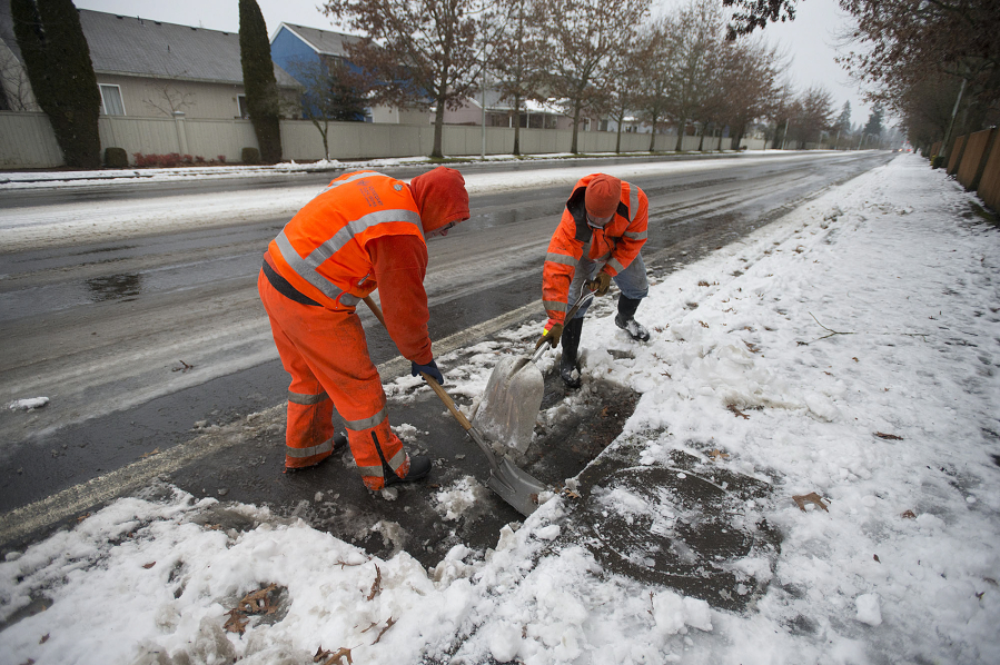 Howard Taylor, left, and Gavin Craig of the Vancouver Department of Public Works stormwater division clear snow from storm drains along Southeast 20th Street on Tuesday afternoon. Top, a pedestrian on Tuesday afternoon navigates an icy street made more slippery by a thin layer of freezing rain in southeast Vancouver.