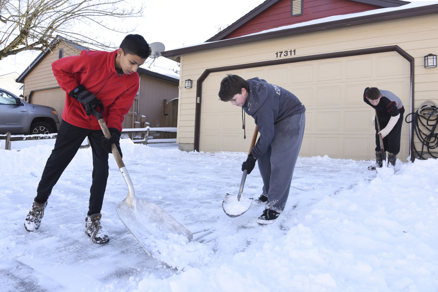 Dhruv Desai, 13, from left, Randall Conner, 10, and Greg Conner, 13, shovel the snow off a neighbor&#039;s driveway near Southeast 19th Street and Southeast 173rd Avenue in Vancouver on Thursday.