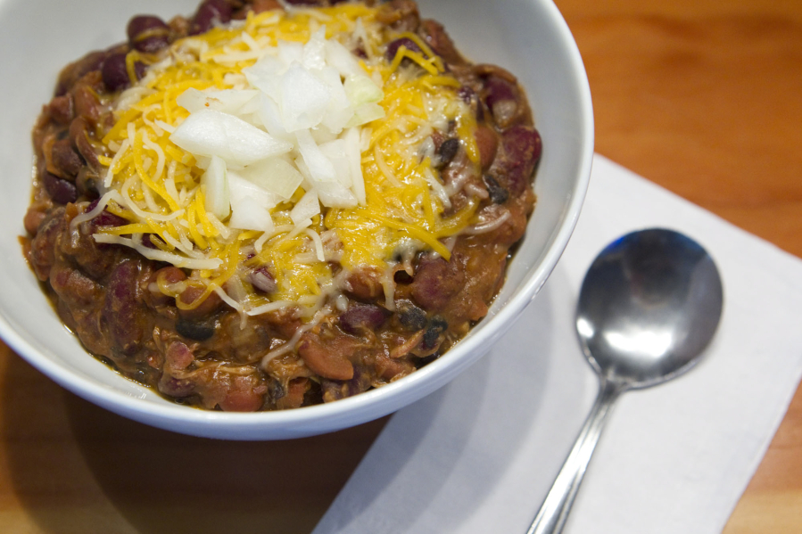 A bowl of red chili with beans, beef, cheese and onions.
