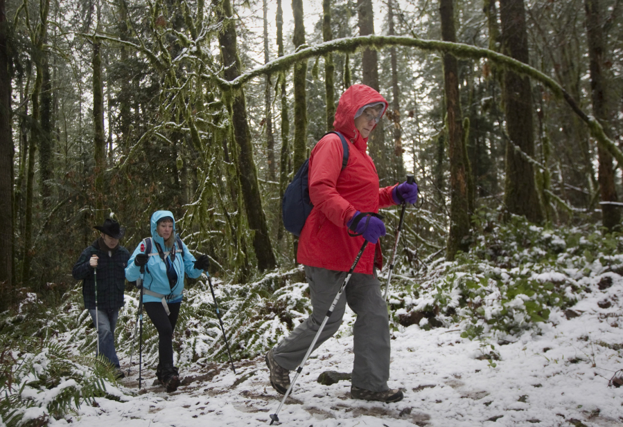 Carol Whitaker uses poles for balance as she walks though a snowy patch on a guided hike Sunday afternoon at Battle Ground Lake State Park. Behind her are Junelle Lawry and her husband, Don Lawry.