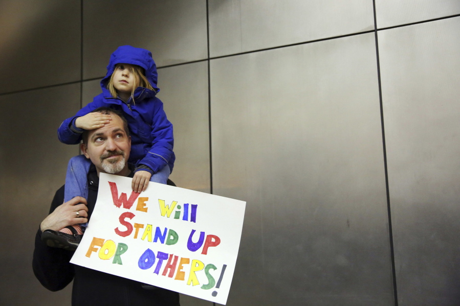 Matt Sernett and his daughter Wade, 5, join more than 1,000 protesters Saturday at Seattle-Tacoma International Airport.