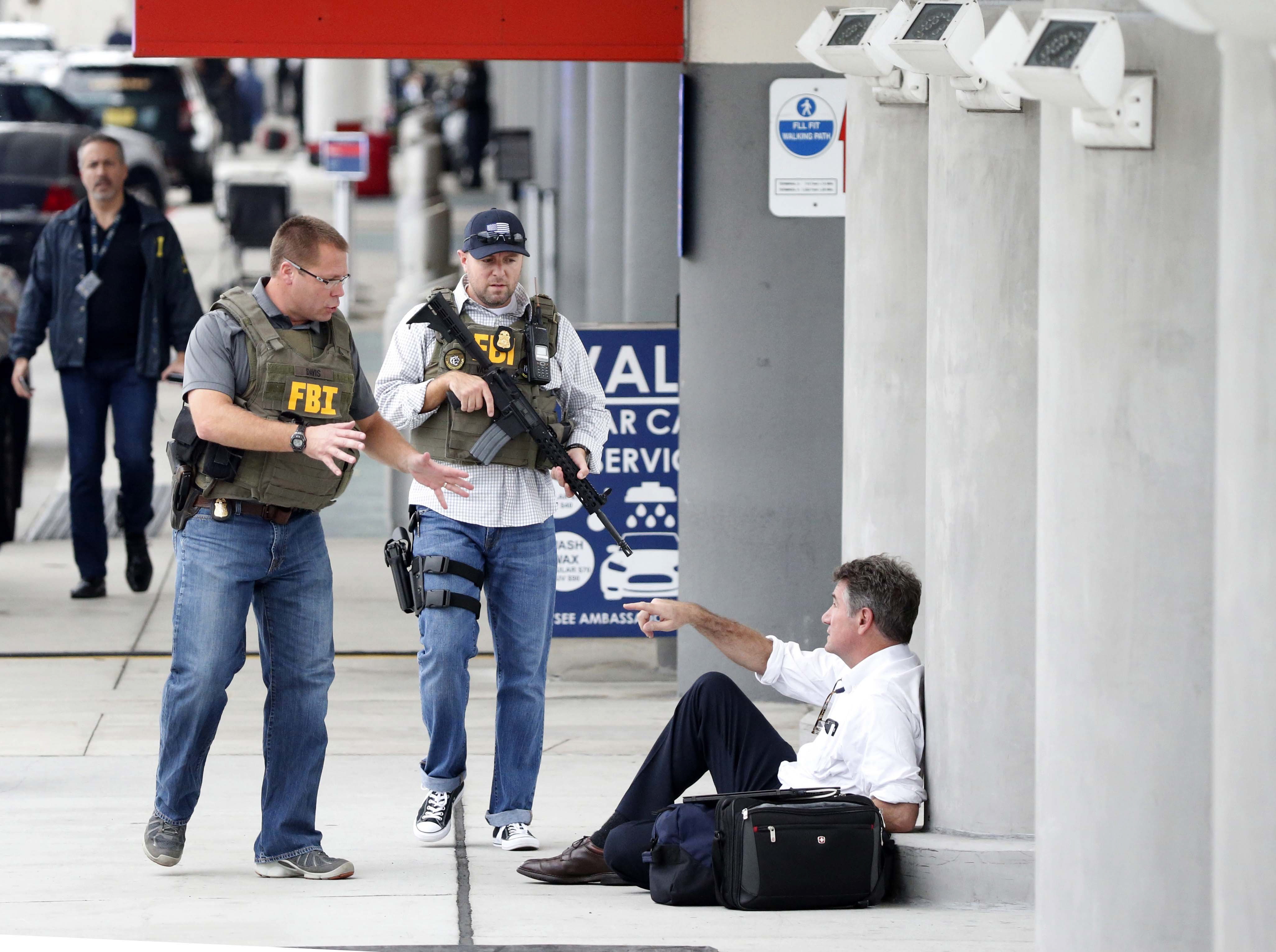 A law enforcement officers talk to a man at Fort LauderdaleÄìHollywood International Airport, Friday, Jan. 6, 2017, in Fort Lauderdale, Fla.   A gunman opened fire in the baggage claim area at the airport Friday, killing several people and wounding others before being taken into custody in an attack that sent panicked passengers running out of the terminal and onto the tarmac, authorities said.