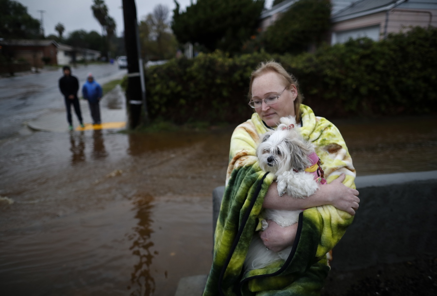 A woman who gave her name as Julie holds her dog, Shana, as they wait outside of her office after rainwater flooded the street Friday in San Diego.