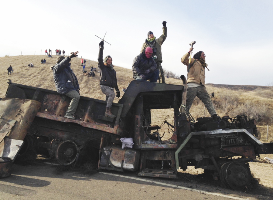 Protesters against the Dakota Access oil pipeline stand on a burned-out truck near Cannon Ball, N.D., that they removed from a long-closed bridge a day earlier on a state highway near their camp. Police allege in court filings that opponents of the oil pipeline made threats against officers and public officials in North Dakota last year, prompting additional security for the state&#039;s governor. The filings are part of a lawsuit filed in November by pipeline protesters who accuse police of excessive force in the Nov. 20 clash over a blockaded bridge.