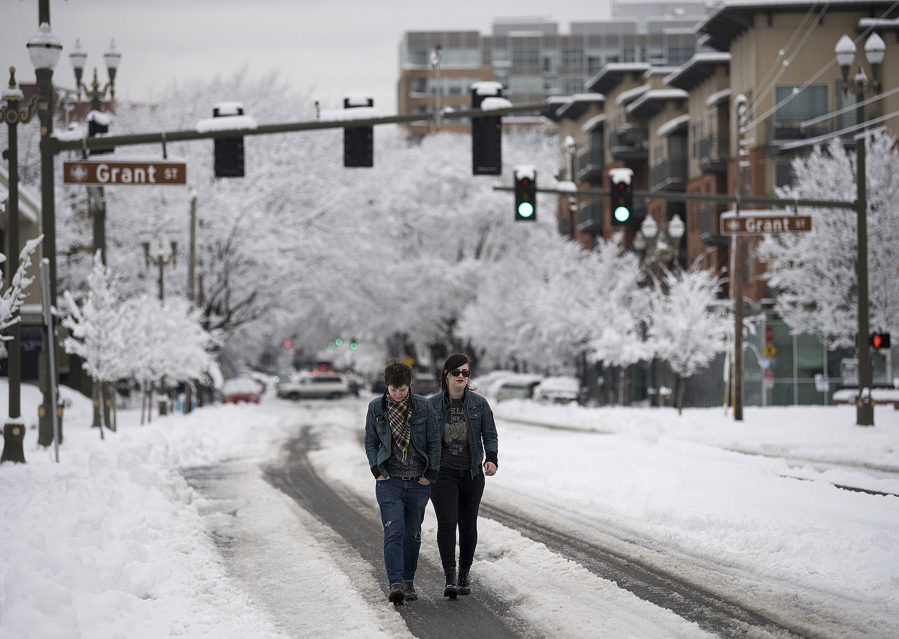 Cassiopeia Rivera, left, and McKenzie Prior walk through the streets in downtown Vancouver Wednesday afternoon. Many sidewalks in the city are still choked with snow.
