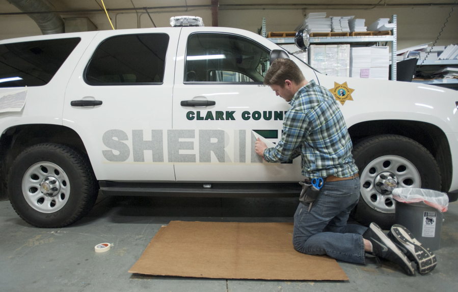 Kai Crown applies decals to sheriffs&#039; office vehicles at International Graphics and Nameplate in Vancouver.