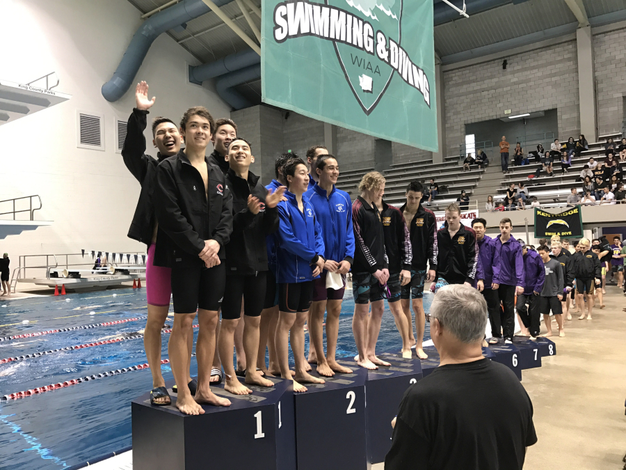 Mark Kim waves to the crowd as he stands with the other members of Camas’ 200 free relay team — Eric Wu, Jaden Kim and Tom Utas — that won a state championship on Saturday.