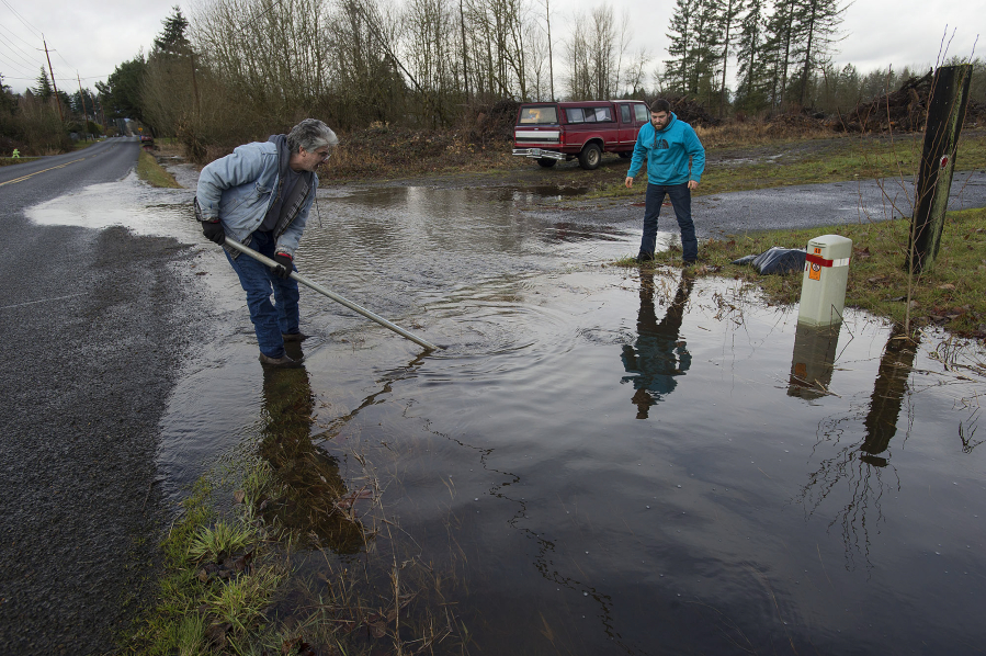 Battle Ground&#039;s Frank Alarcon, left, tries Monday to dislodge a garbage can blocking a drainage ditch in front of his home with the help of passer-by Herschel Gaskill in northeast Battle Ground. They succeeded, and water started to drain properly.