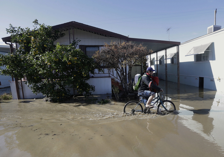 A man rides a bicycle down a flooded street in South Bay Mobile Home Park in San Jose, Calif., on Wednesday. Rising floodwaters sent thousands of residents fleeing inundated homes in San Jose and forced the shutdown of a major freeway Wednesday.