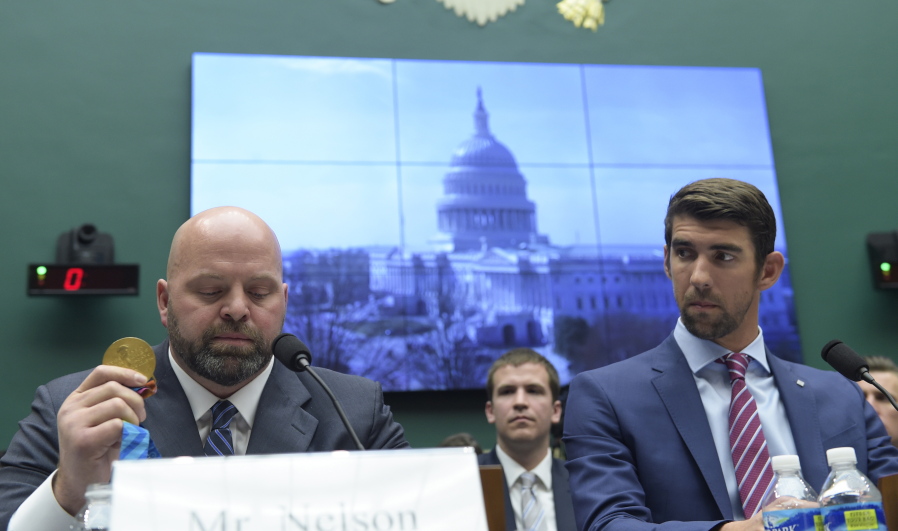 Olympic swimming champion Michael Phelps listens at right as Olympic shot-put champion Adam Nelson holds up his gold medal as they testify on Capitol Hill in Washington on Tuesday before the House Commerce Energy and Commerce subcommittee hearing on the international anti-doping system.