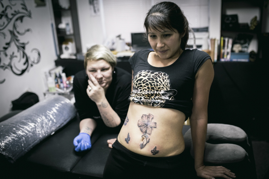 Lyaysan, front, and tattoo artist Yevgeniya Zakhar look in a mirror Dec. 6 in Ufa, Russia, at the tattoos Lyaysan got to conceal a scar from a domestic violence attack.