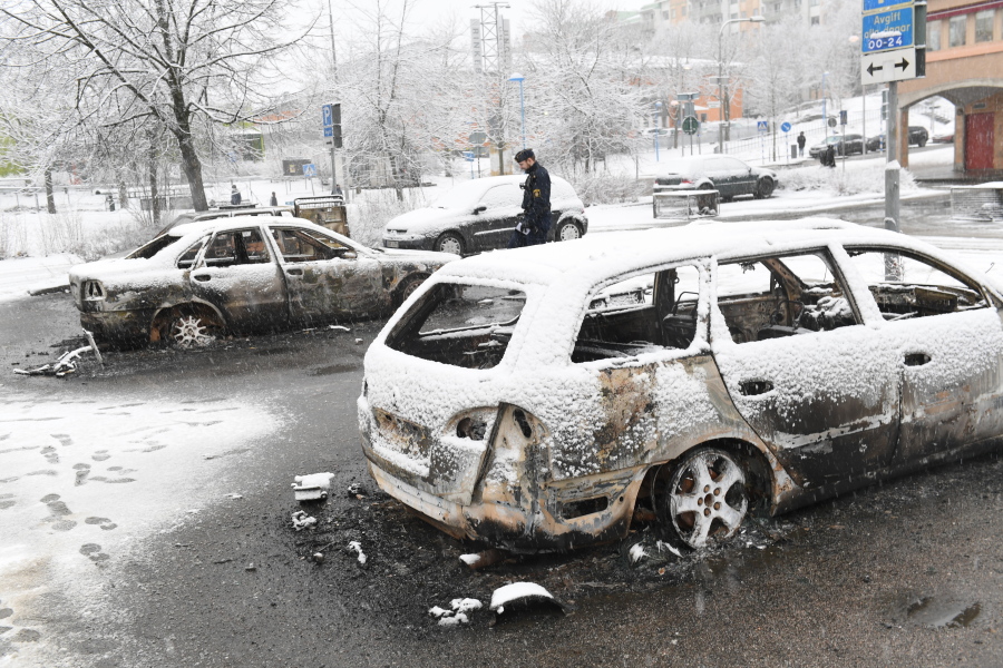 A policeman investigates a burned-out car Tuesday in the suburb Rinkeby outside Stockholm. Swedish police on Tuesday were investigating a riot that broke out Monday night in a predominantly immigrant suburb in Stockholm after officers arrested a suspect on drug charges.