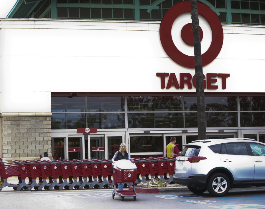 A woman pushes her shopping cart as an employee pulls a long line of carts outside a Target in Encinitas, Calif.