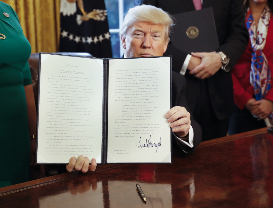 President Donald Trump holds up an executive order on reviewing the 2010 Dodd-Frank financial oversight law after he signed the order Friday in the Oval Office.