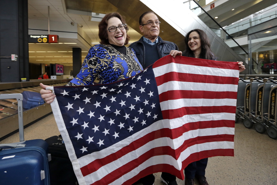 Jayne Novak, left, smiles as she stands with her husband, Allen Novak, newly-arrived from Iran, and their daughter Nikta, as they stand with a flag and pose for cameras Monday at Seattle Tacoma International Airport in SeaTac. Allen Novak joined his family of Silverdale on a conditional resident visa. Washington Gov. Jay Inslee, Attorney General Bob Ferguson and Port of Seattle Commissioner President Tom Albro joined family members Monday to welcome another immigrant, Isahaq Ahmed Rabi, who was blocked from entry last week due to President Donald Trump&#039;s immigration order.