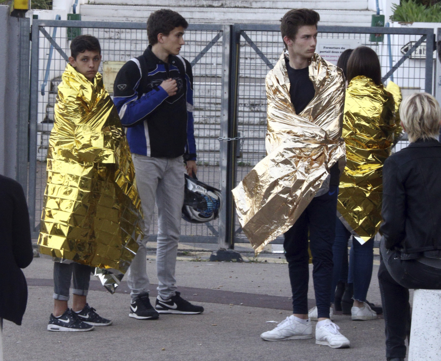 Students wrapped in blankets wait Thursday near their high school in Grasse, France, after a 16-year-old student opened fire, wounding two other students and the principal who was trying to intervene.