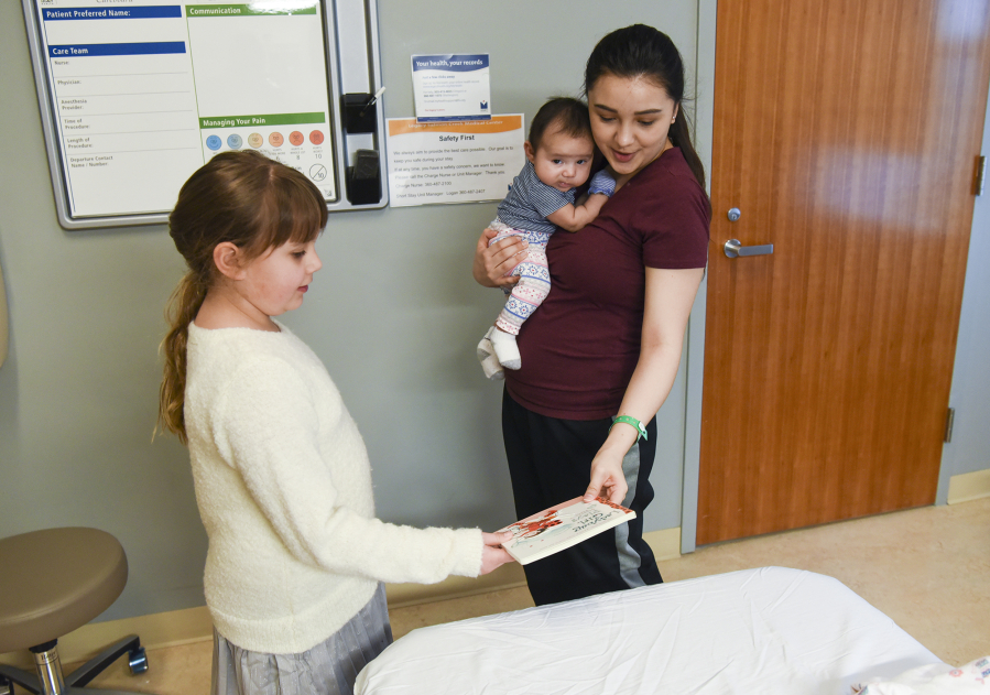 Kamryn Reilly, 8, donates the book &quot;Ladybug Girl Plays&quot; to 9-week-old Lucy Pimentel, held by her mother, Cammy Torres, at Legacy Salmon Creek Medical Center.
