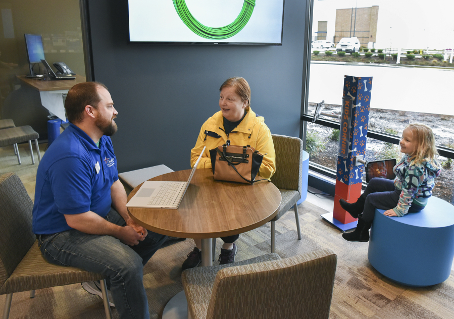 TwinStar Credit Union Branch Manager Jeff Tennant helps customer Tammie Ferrell while her granddaughter plays at the bank&#039;s &quot;Kids Corner.&quot; Banks are becoming more automated and supplying more amenities as online and mobile banking becomes more popular.
