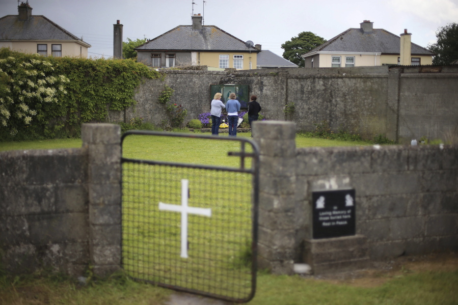 People gather June 7, 2014, at the site of a mass grave for children who died in the Tuam mother and baby home, in Tuam, County Galway. Forensics experts say they have found a mass grave for young children at a former Catholic orphanage in Ireland where suspicions of unrecorded, unmarked burials have lingered for decades.