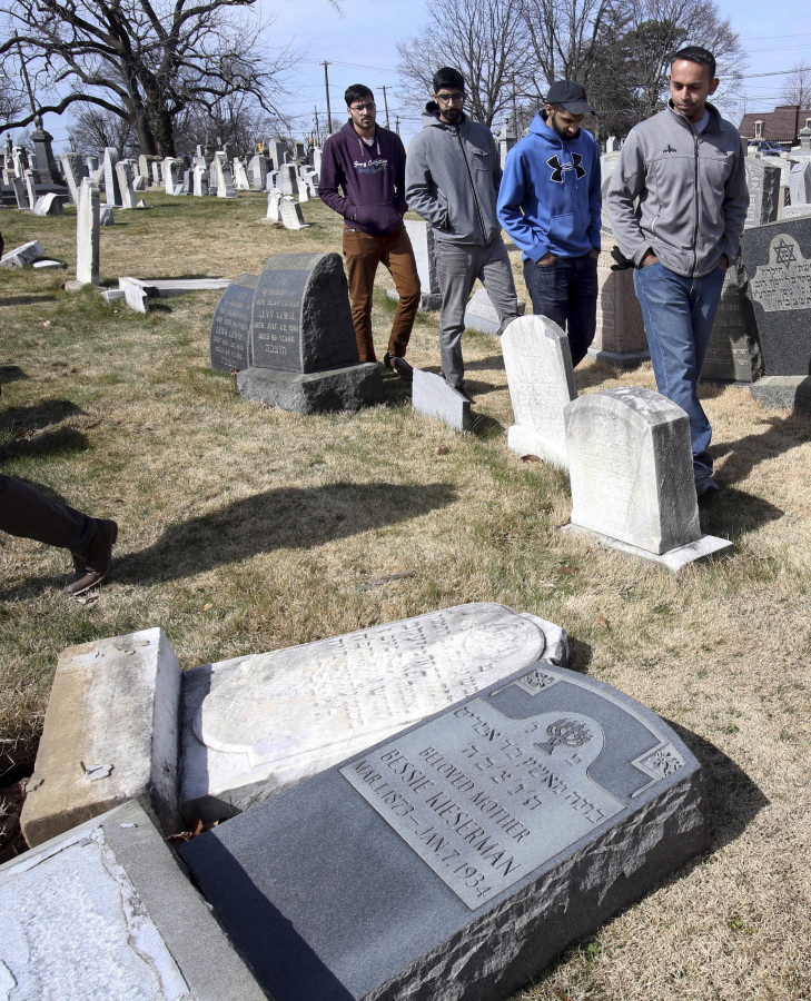 Volunteers from the Ahmadiyya Muslim Community survey damaged headstones at Mount Carmel Cemetery in Philadelphia. More than 100 headstones have been vandalized at the Jewish cemetery, discovered less than a week after similar vandalism in Missouri, authorities said.