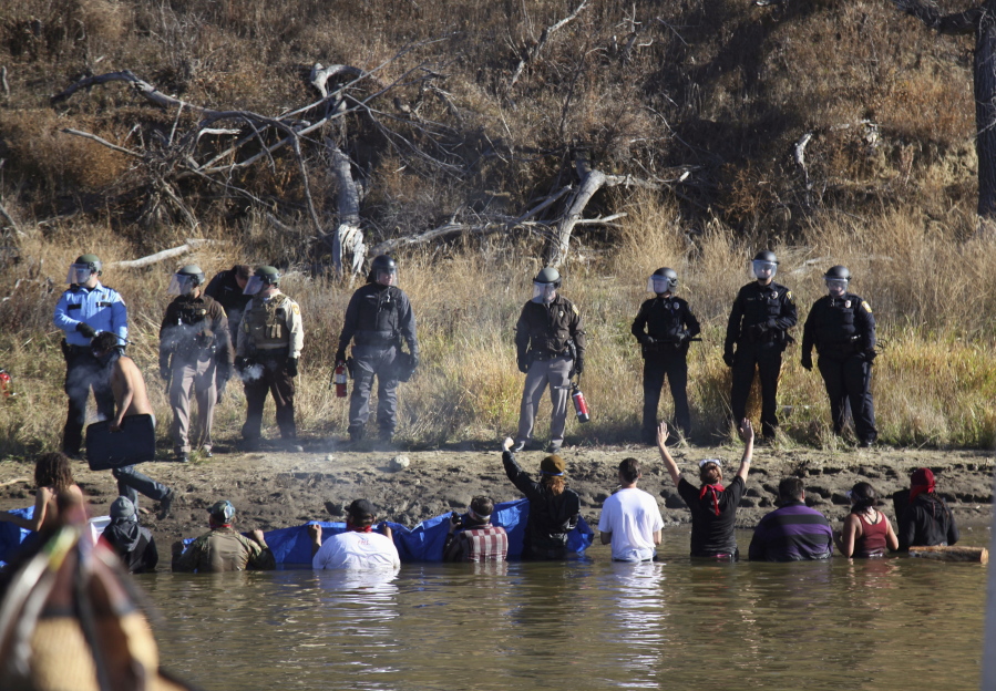 FILE - In this Nov. 2, 2016, file photo, protesters demonstrating against the expansion of the Dakota Access pipeline wade in cold creek waters confronting local police near Cannon Ball, N.D. North Dakota officials appear poised to go after the U.S. government ??? and thus U.S. taxpayers ??? to recoup more than $38 million in state expenses related to months of protests against the Dakota Access pipeline. (AP Photo/John L.