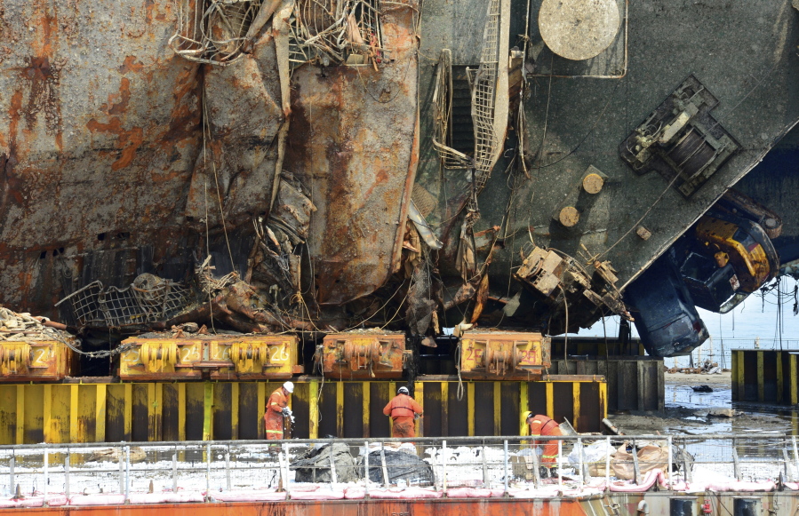 Workers fasten the sunken ferry Sewol to a semi-submersible transport vessel in waters off Jindo, South Korea, on Tuesday. South Korea has held a memorial ceremony at sea for the nine passengers still missing from the 2014 ferry disaster that killed 304 passengers near the ship&#039;s wreckage that was raised from the waters last week.