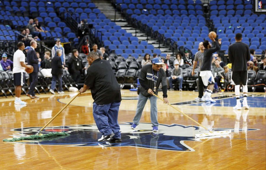 Minnesota Timberwolves&#039; Andrew Wiggins, back right, practices as Target Center workers wipe down the wet basketball floor prior to the NBA basketball game against the Portland Trail Blazers Monday, March 6, 2017, in Minneapolis. High humidity in Minneapolis and condensation from ice underneath the basketball court for upcoming ice-centered events contributed to the wet floor.